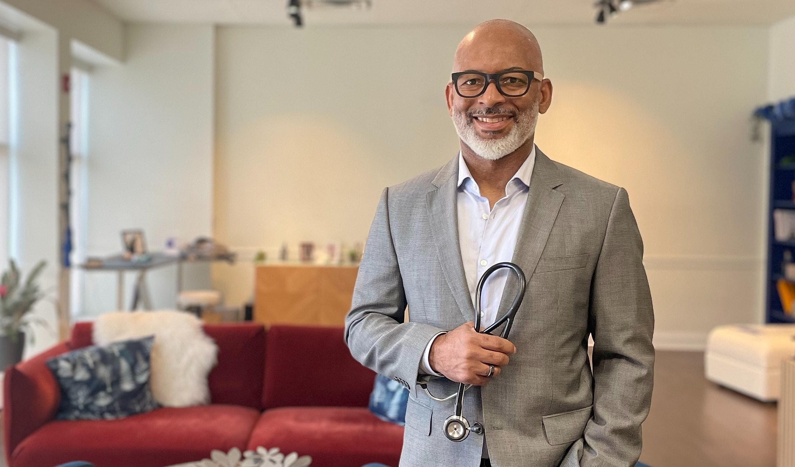 Man in formal suit smiling against brick wall.