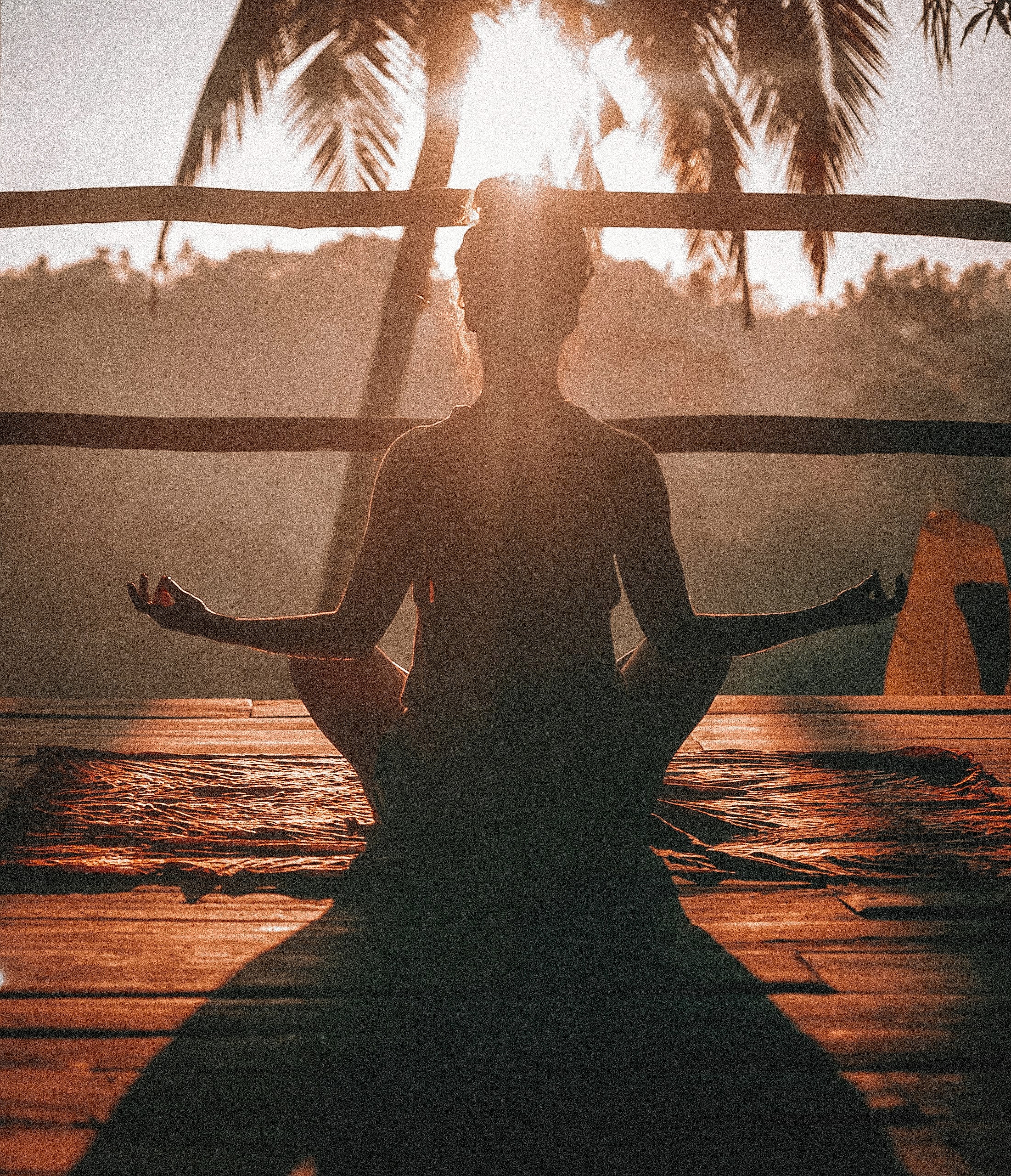 Person meditating at sunrise surrounded by nature.